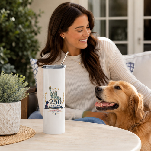 Lifestyle image of white 250 Years USA stainless steel tumbler on a table beside a woman and golden retriever.