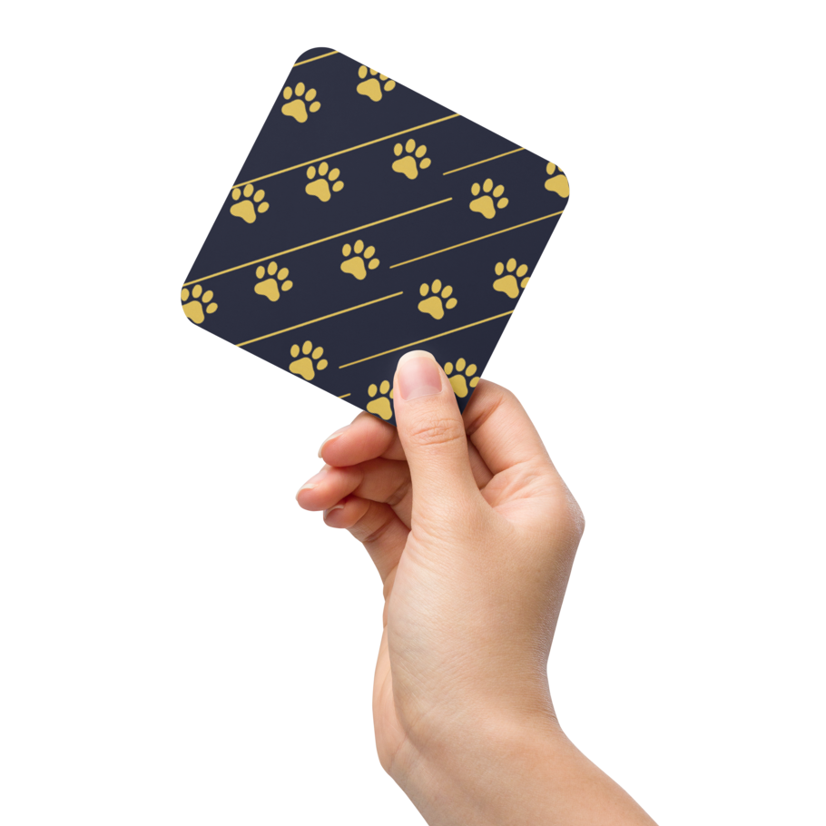 Hand holding a blue coaster with gold paw prints on a white background