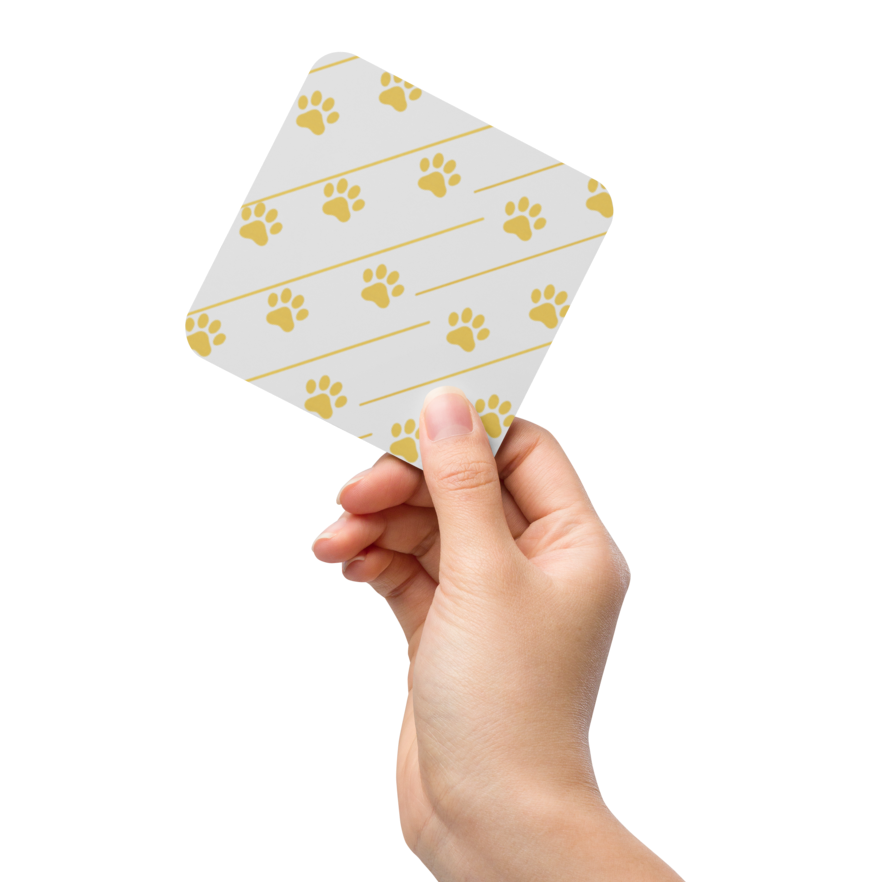 Hand holding a small ivory whisper coaster with gold paw print pattern on a white background