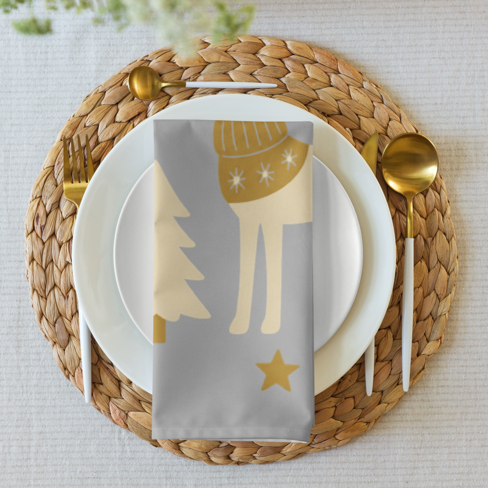 A styled table setting featuring a silver napkin with a gold holiday deer pattern, layered over white plates and cutlery.