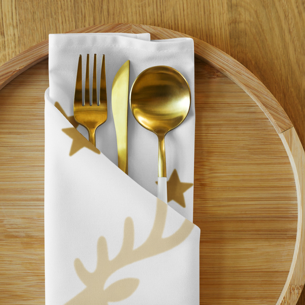 Gold-toned flatware, including a fork, knife, and spoon, arranged on a white napkin with a gold reindeer print, set on a round wooden serving tray.