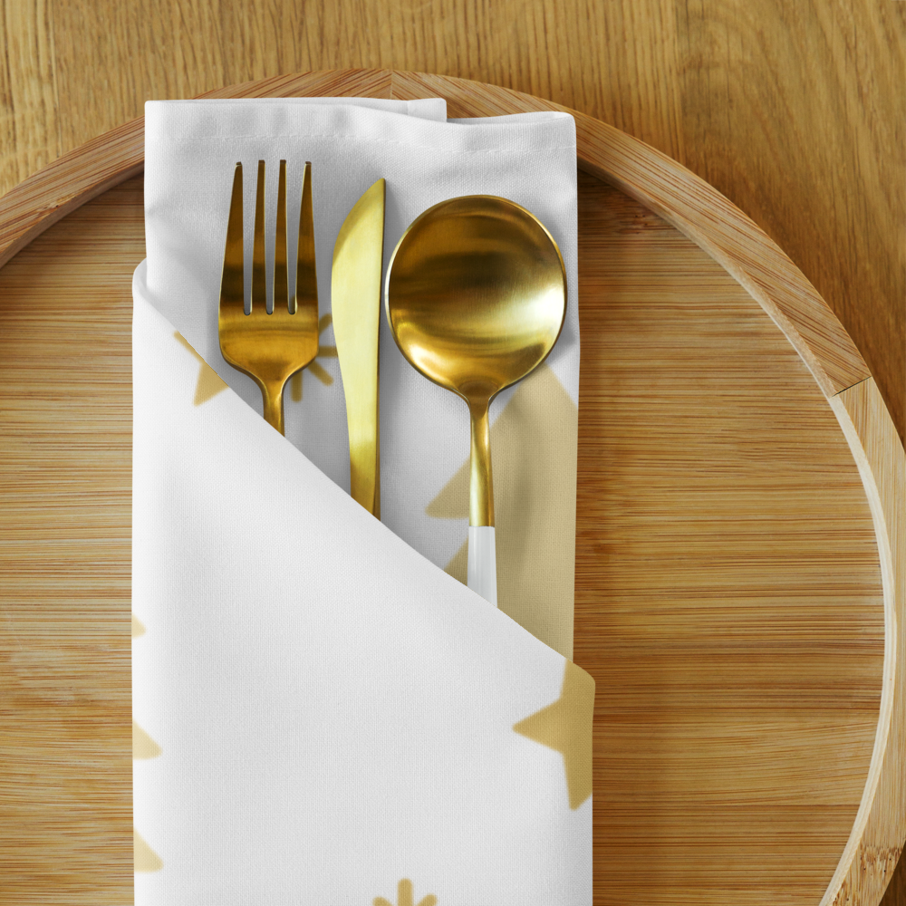 A white cloth napkin with gold trees accents on a round wooden serving tray and Gold-toned flatware. 