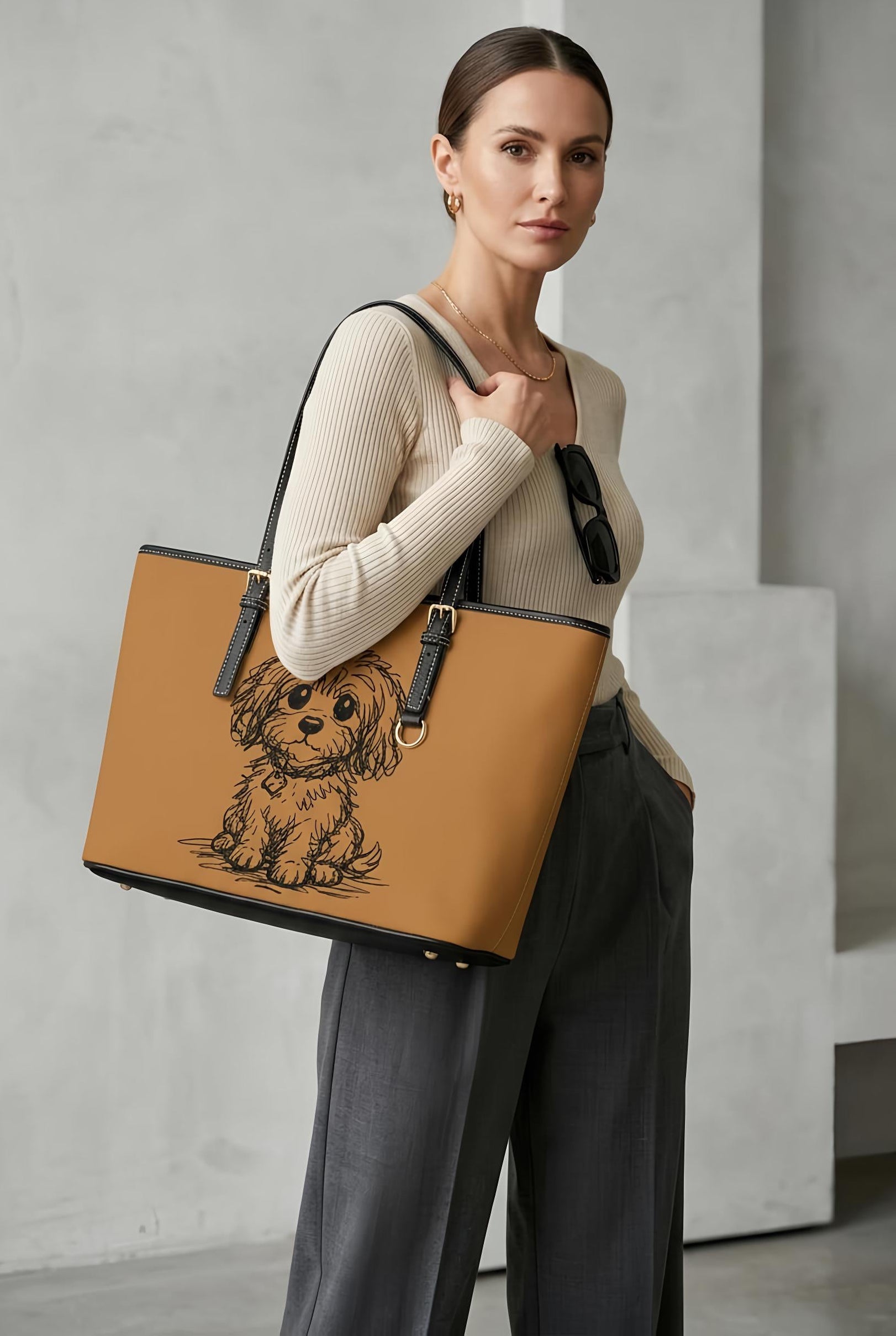 Woman holding a tan tote bag with a dog illustration against a gray concrete wall.