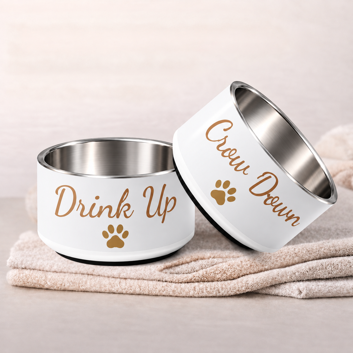Customizable ivory stainless steel dog bowls with text 'Drink Up’ and ‘Chow Down’ with small gold paw prints.