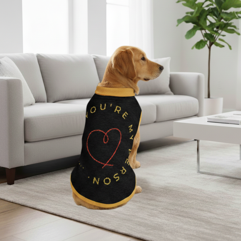 Dog wearing a black shirt with a red heart and text in a living room.
