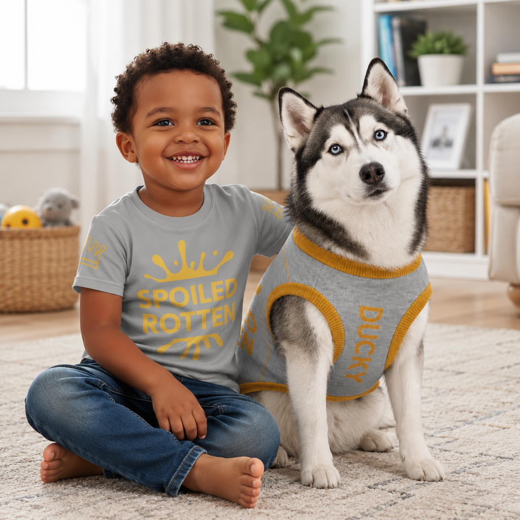 Boy wearing the unisex "Spoiled Rotten" shirt with a dog wearing the "Spoiled Rotten" Sweater matching set sitting on the floor with candy and toys, by Uncommon Canine Couture Co.