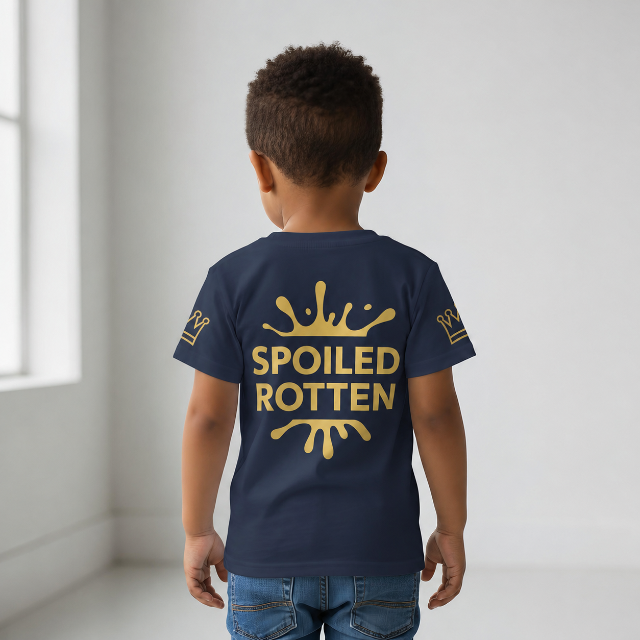 Back view of child wearing navy Spoiled Rotten T-shirt with a graphic gold splash design and gold crowns on sleeve