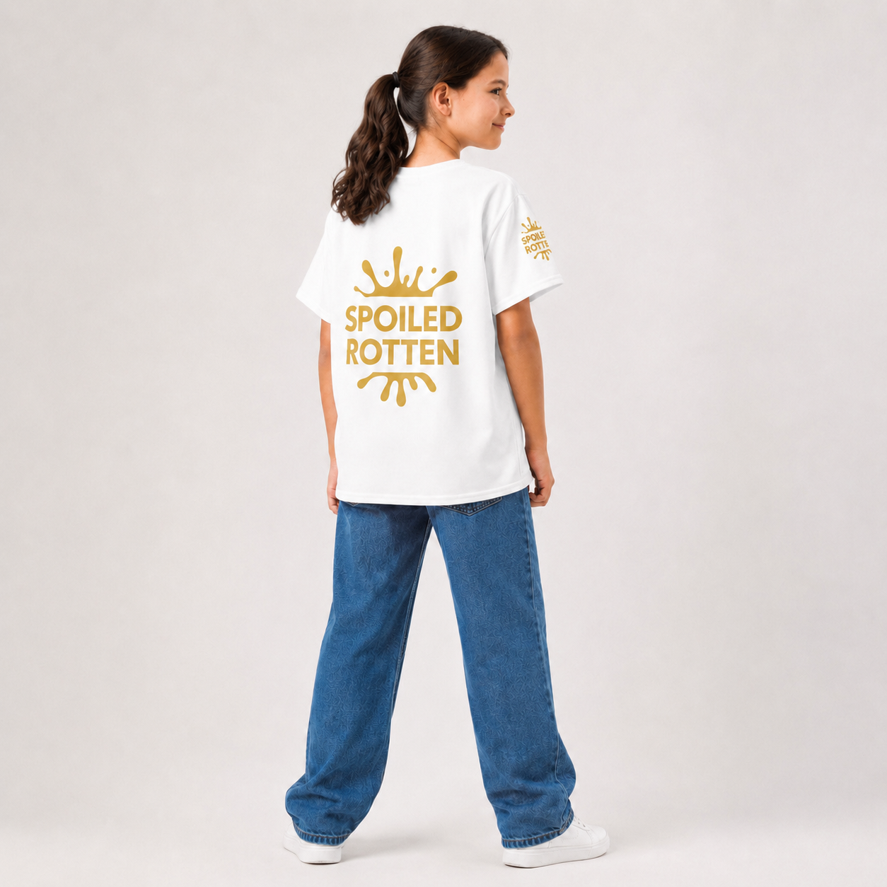 A young girl size 16 is shown from the back wearing a white t-shirt with a gold 'SPOILED ROTTEN' graphic standing against a light gray studio background.