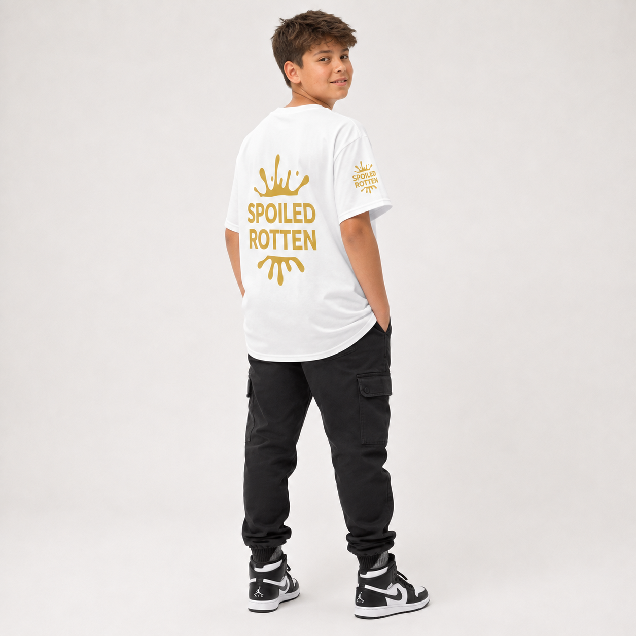 A boy modeling a unique white t-shirt from the back, with a gold splash graphic and the text 'SPOILED ROTTEN'. against a light gray studio background.