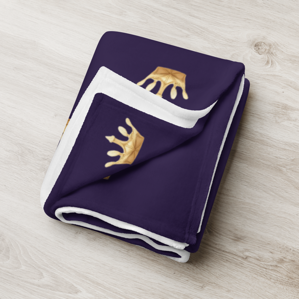 Folded purple blanket with gold crowns on a light wooden surface