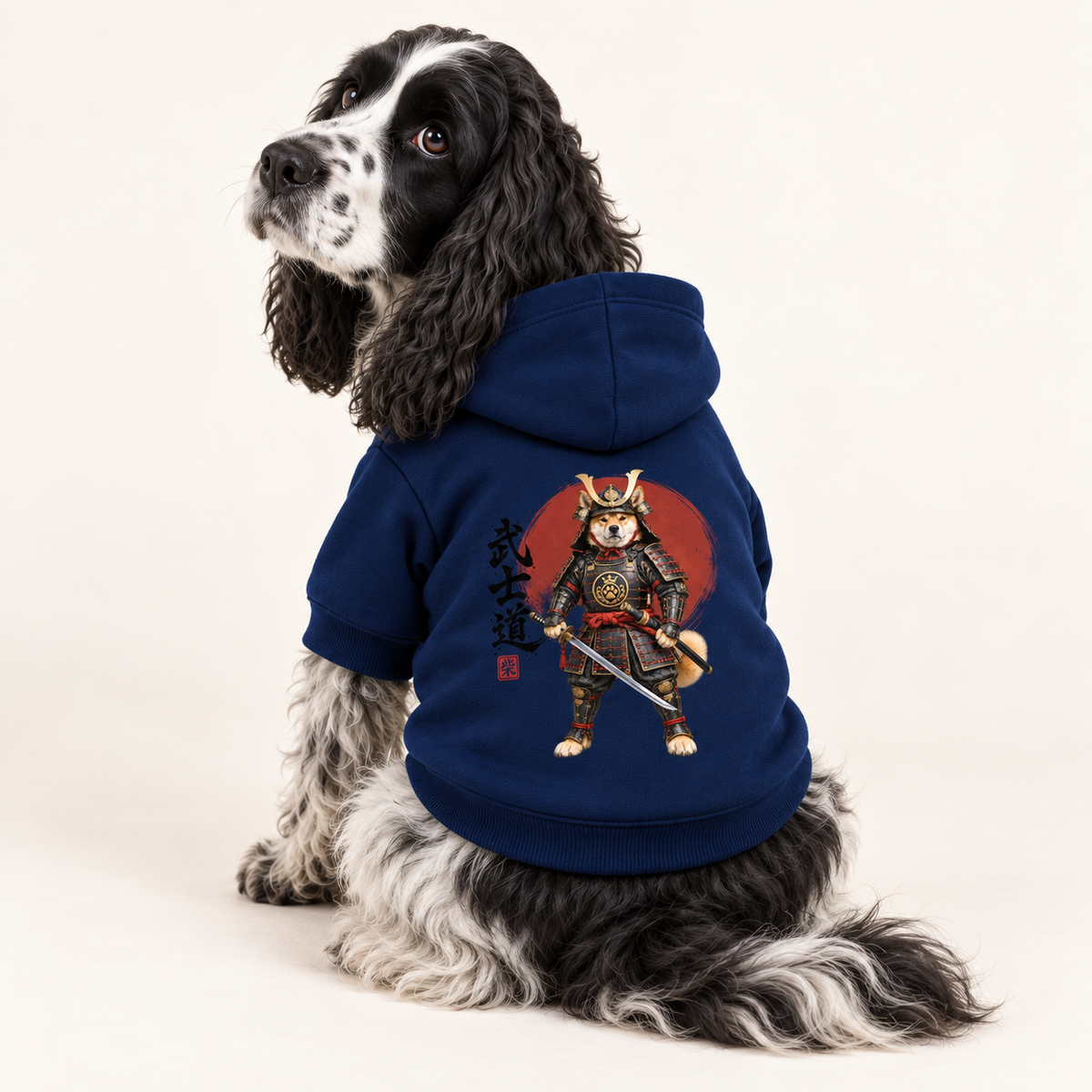 A black and white dog wearing a navy blue hoodie with a samurai dog graphic on the back, photographed against a white studio background.