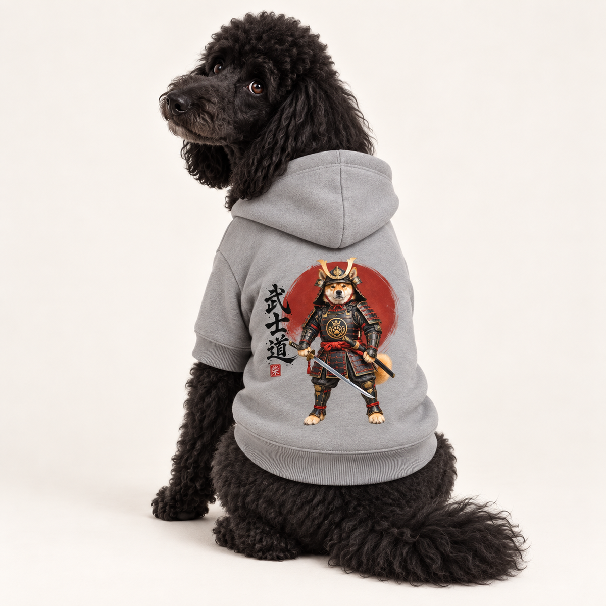 A dog wearing a gray hoodie with a colorful samurai dog graphic and Japanese text, against a white studio background.